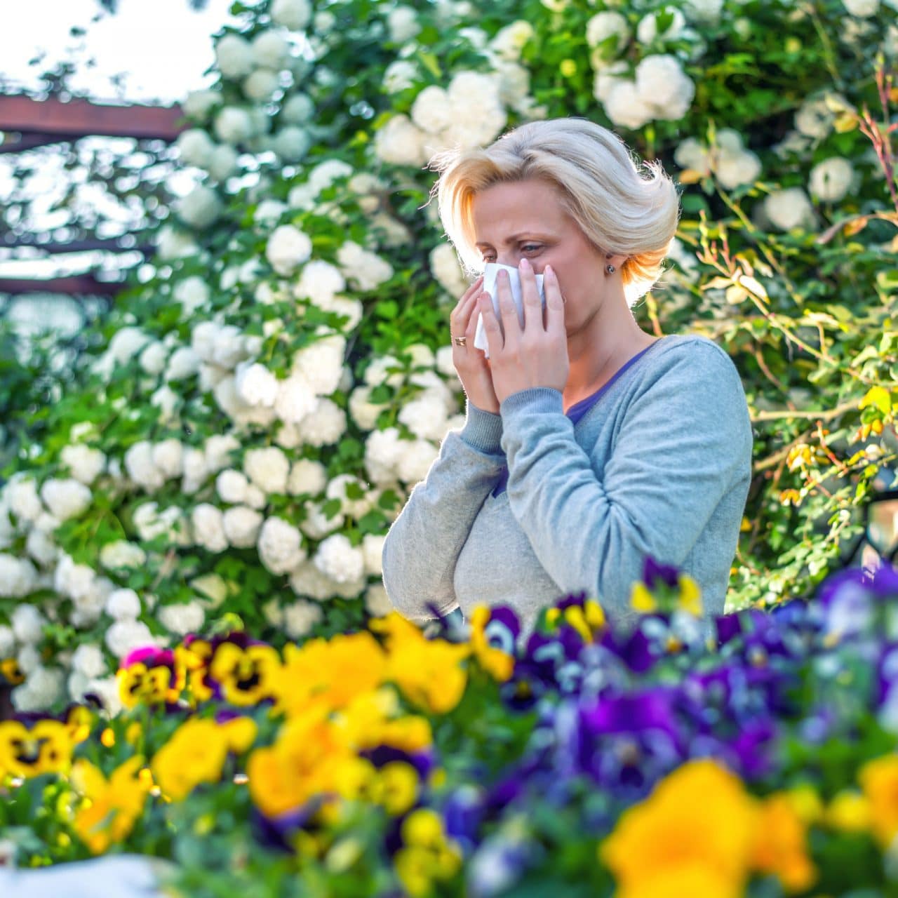 A person standing in a flower garden and blowing their nose
