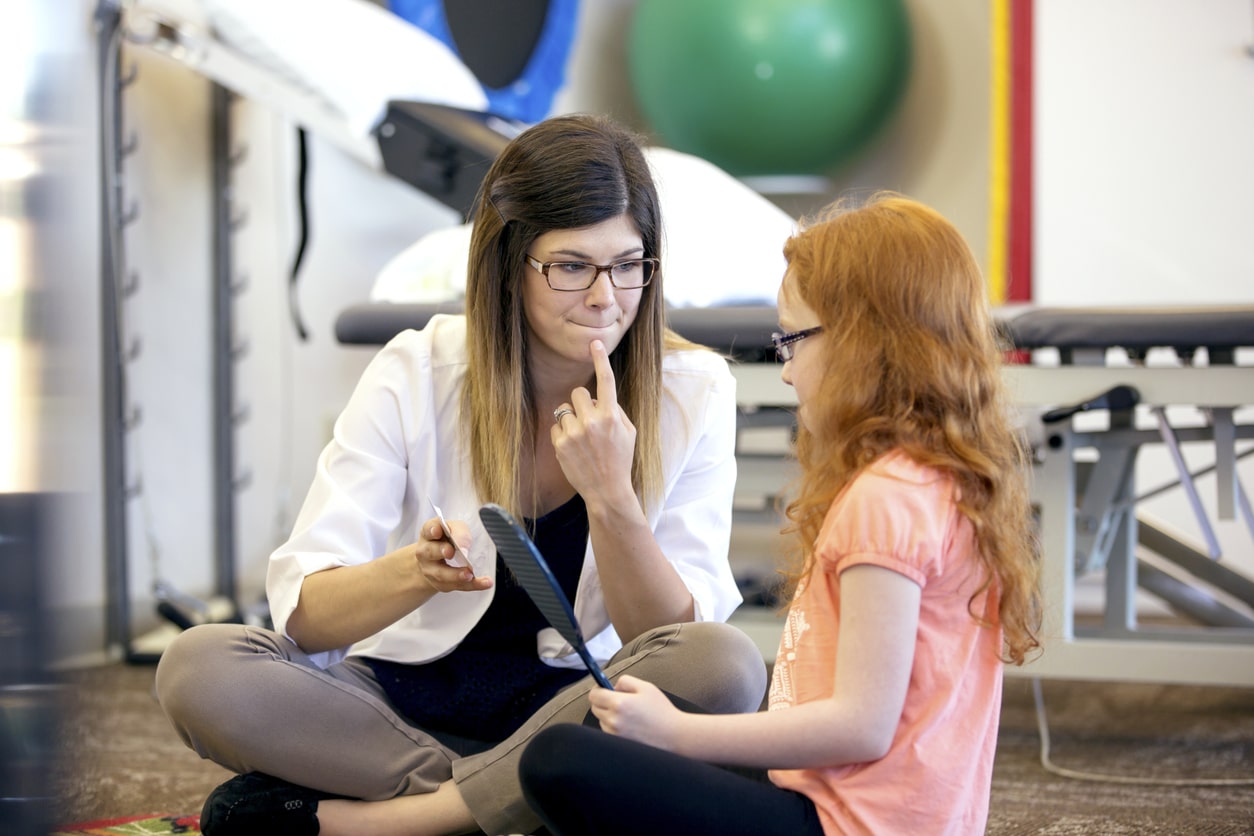A speech therapist pointing to their own face while working with a child