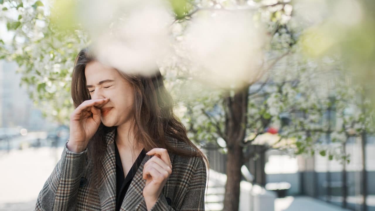 Woman sneezing near the trees.