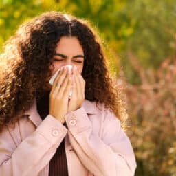 Woman with allergies blows nose in park
