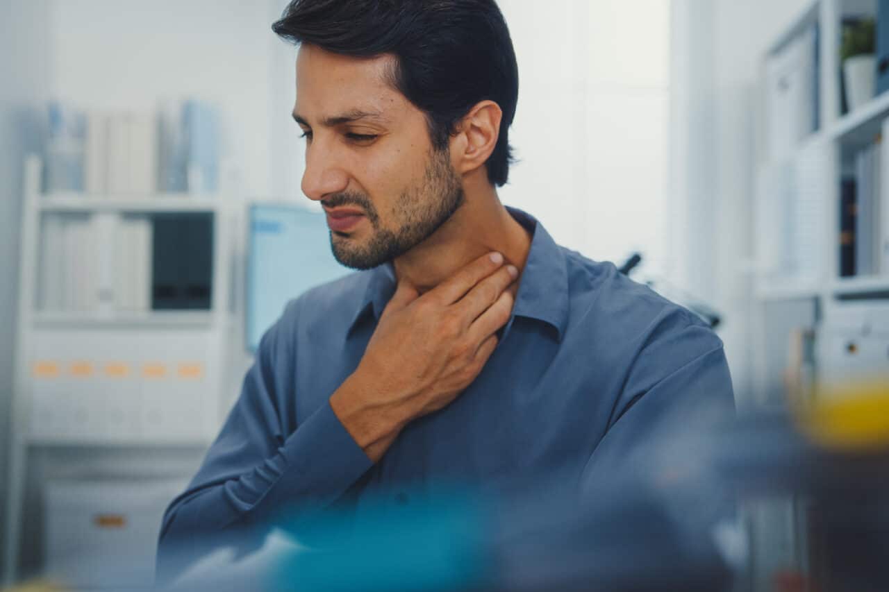 Man holds his hand up to his throat due to throat pain.