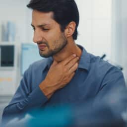 Man holds his hand up to his throat due to throat pain.