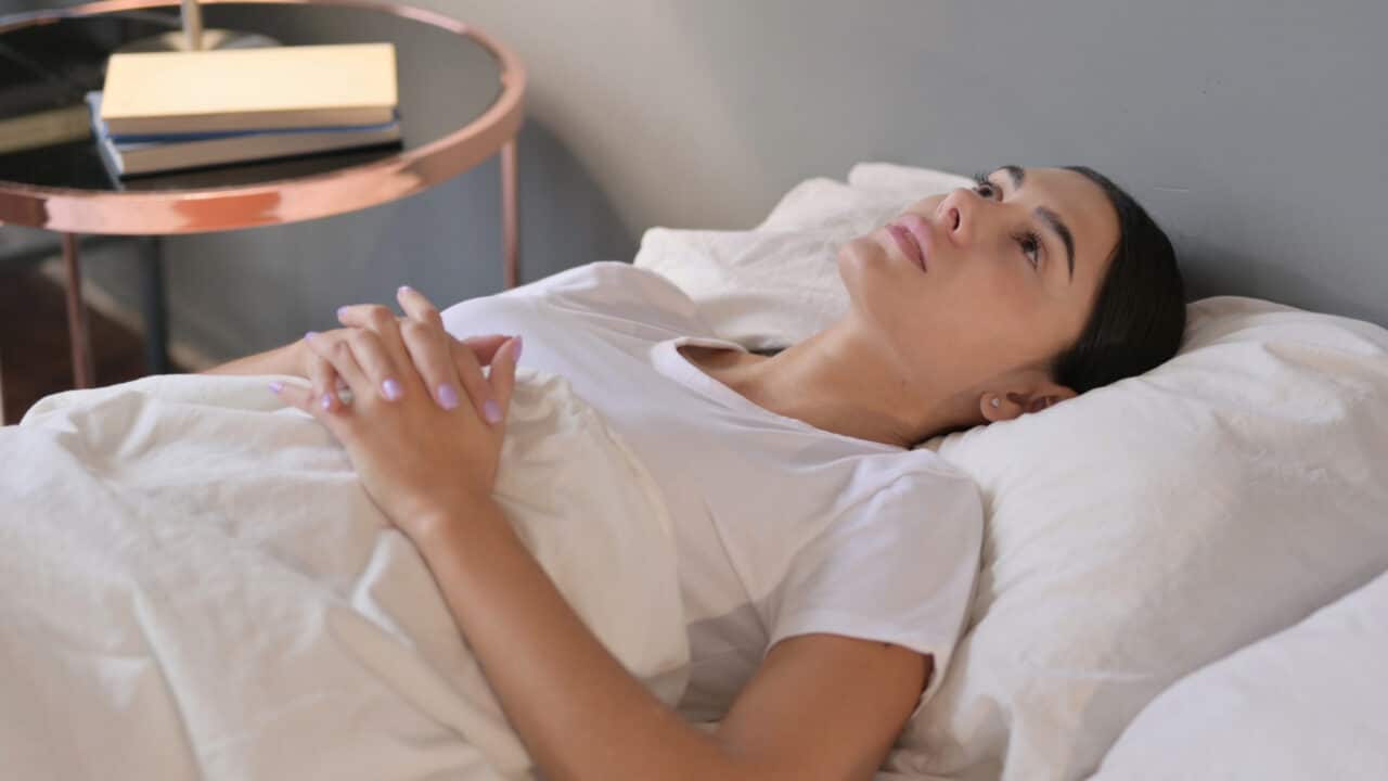 Woman lies awake in bed, having trouble sleeping due to a sore throat.