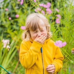 Child with allergies sneezing in a garden on a rainy spring day.