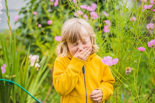 Child with allergies sneezing in a garden on a rainy spring day.